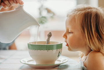 close-up, breakfast, a girl watching her mother pour milk from a jug into a deep plate