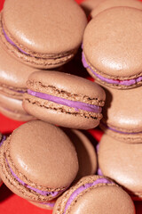 Many chocolate macarons on red background.