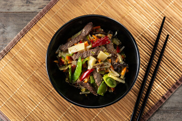 Beef, vegetables and sesame seeds in black bowl. Top view