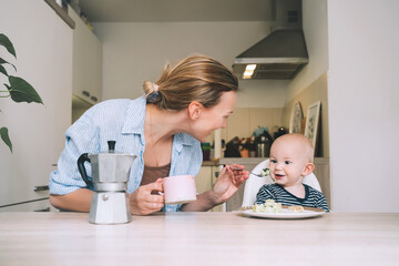 Loving smiling mother and baby eating breakfast and have fun in kitchen at home. Beautiful mother...