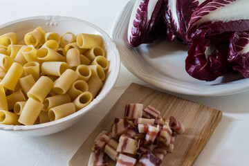 Half sleeves rigate, pasta with bacon and red radicchio. Ingredients still raw, ready to be cooked. White background