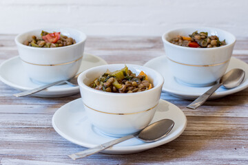 Lentil and escarole soup served in white cups on white wooden background - obrazy, fototapety, plakaty