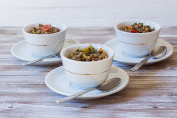 Lentil and escarole soup served in white cups on white wooden background