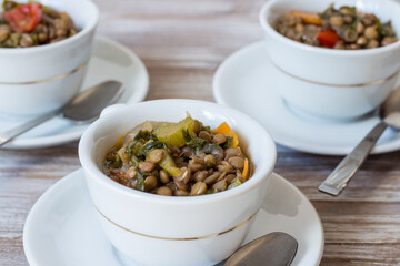 Lentil and escarole soup served in white cups on white wooden background
