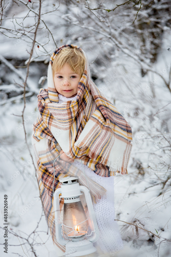 Sticker Beautiful blond toddler child, boy with white knitted handmade overall, holding lantern in the snow