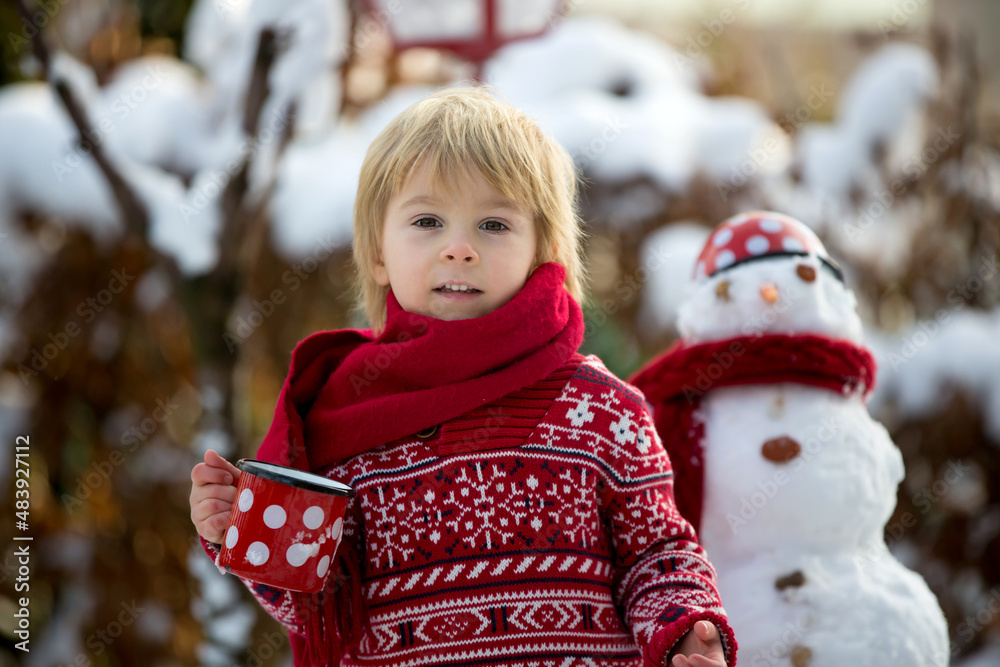 Poster Sweet blond toddler child, boy, playing in garden with snow, making snowman, happy kid winter time