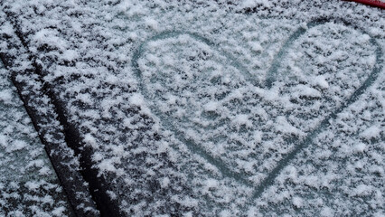 the heart is painted on the fallen snow on the car door glass. side view. a symbol of love on a winter day. february