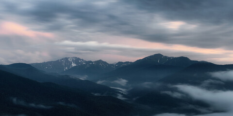 The setting sun illuminates the clouds over the mountain peaks of the caucasus