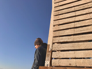 The young man standing near the old wooden wall. One sad depressed person stands near the wall against the clear blue sky backdrop. Background with copy space.