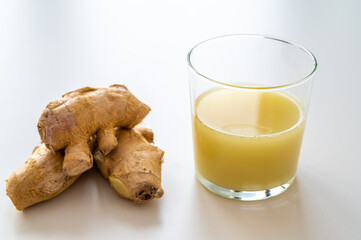 Ginger root, with pieces of ginger next to it and a glass of ginger juice. 