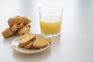 Ginger root, with pieces of ginger next to it and a glass of ginger juice. 