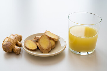 Ginger root, with pieces of ginger next to it and a glass of ginger juice. 