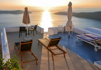 Sun loungers on terrace in the village of Imerovigli with amazing view of sunset over caldera in Santorini, Greece