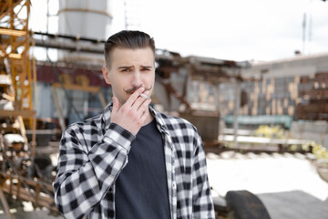 young handsome man with mustache in checkered black and white shirt smoking a cigarette outside....
