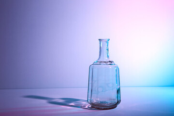 Obraz na płótnie Canvas Glass bottle with copy space. Large creative vintage vase. Graphic still life with light and shadow in multicolor neon light. An art object. Recyclable material. The concept of alcoholism. Open flask.