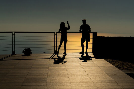 People, a couple of tourists in love on the observation deck in the evening are photographed on the phone against the background of sunset