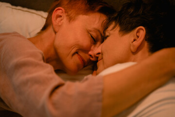 Obraz na płótnie Canvas Mature lesbian couple hugging and smiling while lying in bed