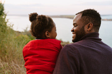Black man smiling and hugging her daughter during walking by river