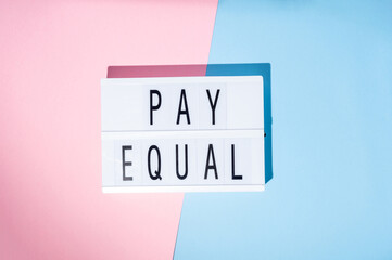 Pay Equal text on the lightbox. Concept of feminism on a blue and pink background. Top view