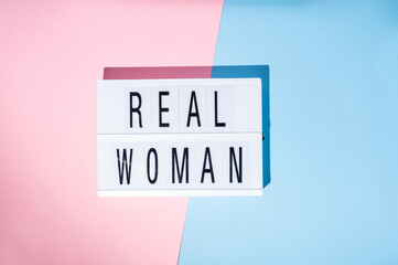 Real Woman text on the lightbox. Concept of feminism on a blue and pink background. Top view