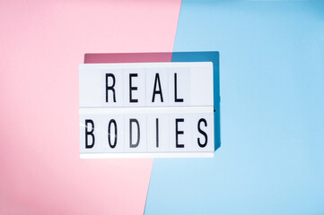 Real Bodies text on the lightbox. Concept of feminism on a blue and pink background. Top view