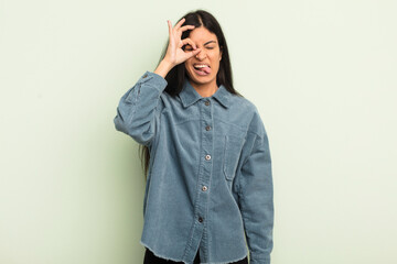 hispanic pretty woman smiling happily with funny face, joking and looking through peephole, spying...