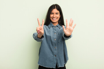 hispanic pretty woman smiling and looking friendly, showing number seven or seventh with hand...