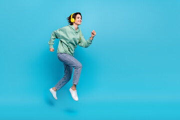 Fototapeta na wymiar Full length profile photo of cute millennial brunette lady run wear headphones pullover jeans footwear isolated on blue background