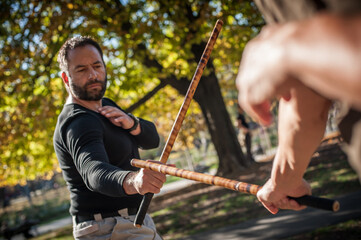 Escrima and kapap instructor demonstrates sticks fighting techniques training methods - obrazy, fototapety, plakaty