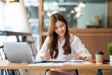 Beautiful young Asian businesswoman smiling sitting working at her workplace at modern office.