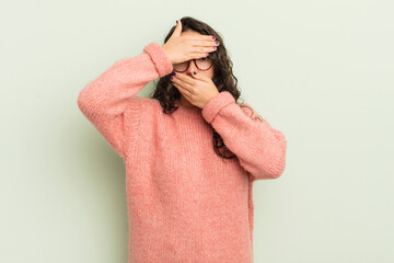 hispanic pretty woman covering face with both hands saying no to the camera! refusing pictures or...