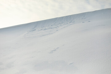 Snowy slope against sky. Avalanche of snow on mountain ridge. Winter weather.