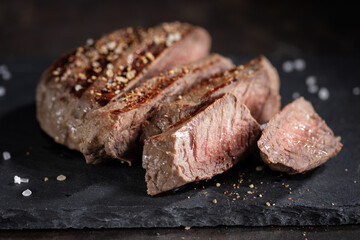 Grilled meat cut in slices on dark slate
