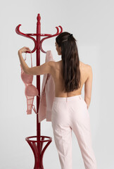 England UK. 2021. Woman getting dressed in pink, bra, jacket by a clothes stand.