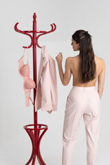 England UK. 2021. Woman getting dressed in pink, bra, jacket by a clothes stand.