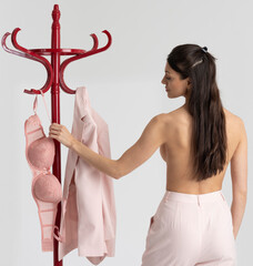 England UK. 2021. Woman getting dressed in pink, bra, jacket by a clothes stand.