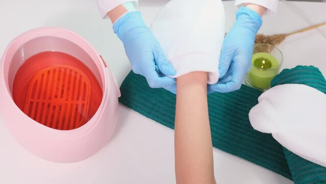  Cosmetologist nail master putting paraffin gloves on the client hands after the paraffin bath for hands at beauty spa salon concept.