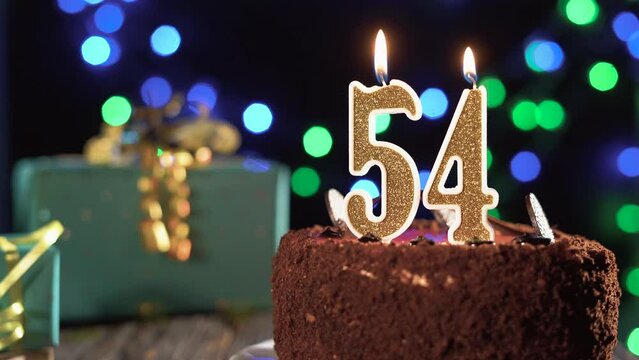 Birthday candle number fifty four on a sweet cake on the table, 54th birthday. Fire from the lighter, blow out the holiday candle.