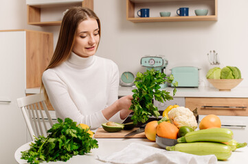 A young, beautiful vegetarian girl or blogger prepares breakfast of fruits, vegetables and greens at home in the kitchen. Blog about healthy eating