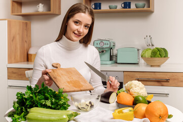 A young, beautiful vegetarian girl or blogger prepares breakfast of fruits, vegetables and greens at home in the kitchen. Blog about healthy eating