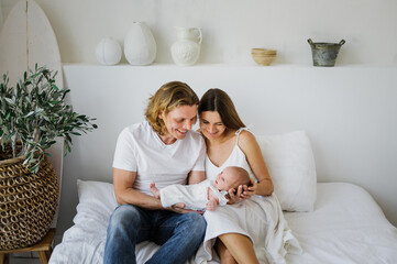 Obraz premium Young mom and dad are holding a newborn in their arms. The family holds a newborn baby girl in their arms.