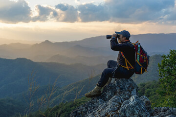Obraz premium Hikers with backpacks holding binoculars sitting on top of the rock mountain