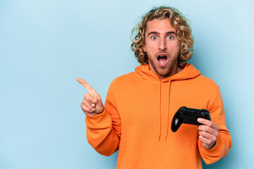 Young caucasian man playing with a video game controller isolated on blue background pointing to...