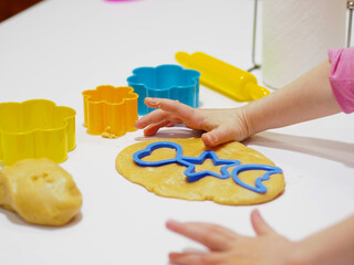 Cute children's hands prepare children's gingerbread cookies in different shapes. Close-up funny child prepares homemade sweet for baking.
