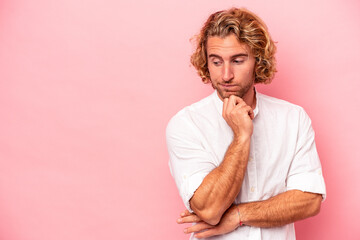 Young caucasian man isolated on pink background looking sideways with doubtful and skeptical expression.