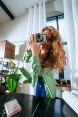 Cheerful young woman making photo on camera at home