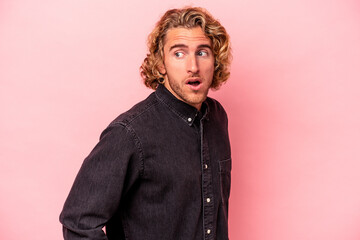 Young caucasian man isolated on pink background looks aside smiling, cheerful and pleasant.