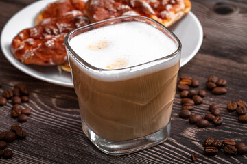 A cup of branded coffee in a scene of coffee beans and a wooden table top. Preparation of cappuccino.