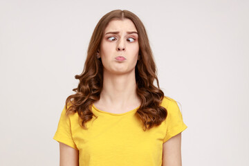 Portrait of attractive funny silly young woman in yellow T- shirt with cross eyed, has stupid dumb...