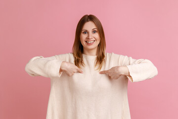 Portrait of blond woman pointing herself and looking at camera with toothy smile, proud of own success, achievement, wearing white sweater. Indoor studio shot isolated on pink background.